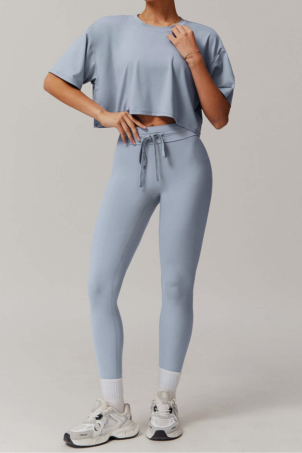 Person wearing a light blue grey athletic outfit with leggings and a crop top on a plain background