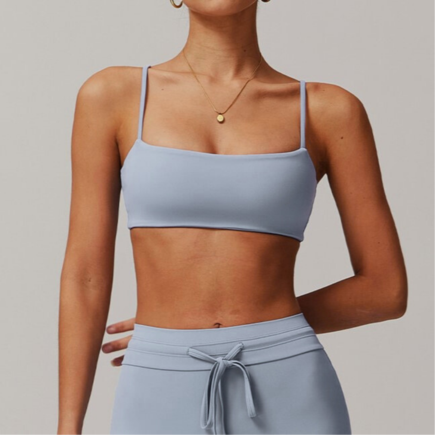 Person wearing a light blue grey sports bra and leggings on a plain background