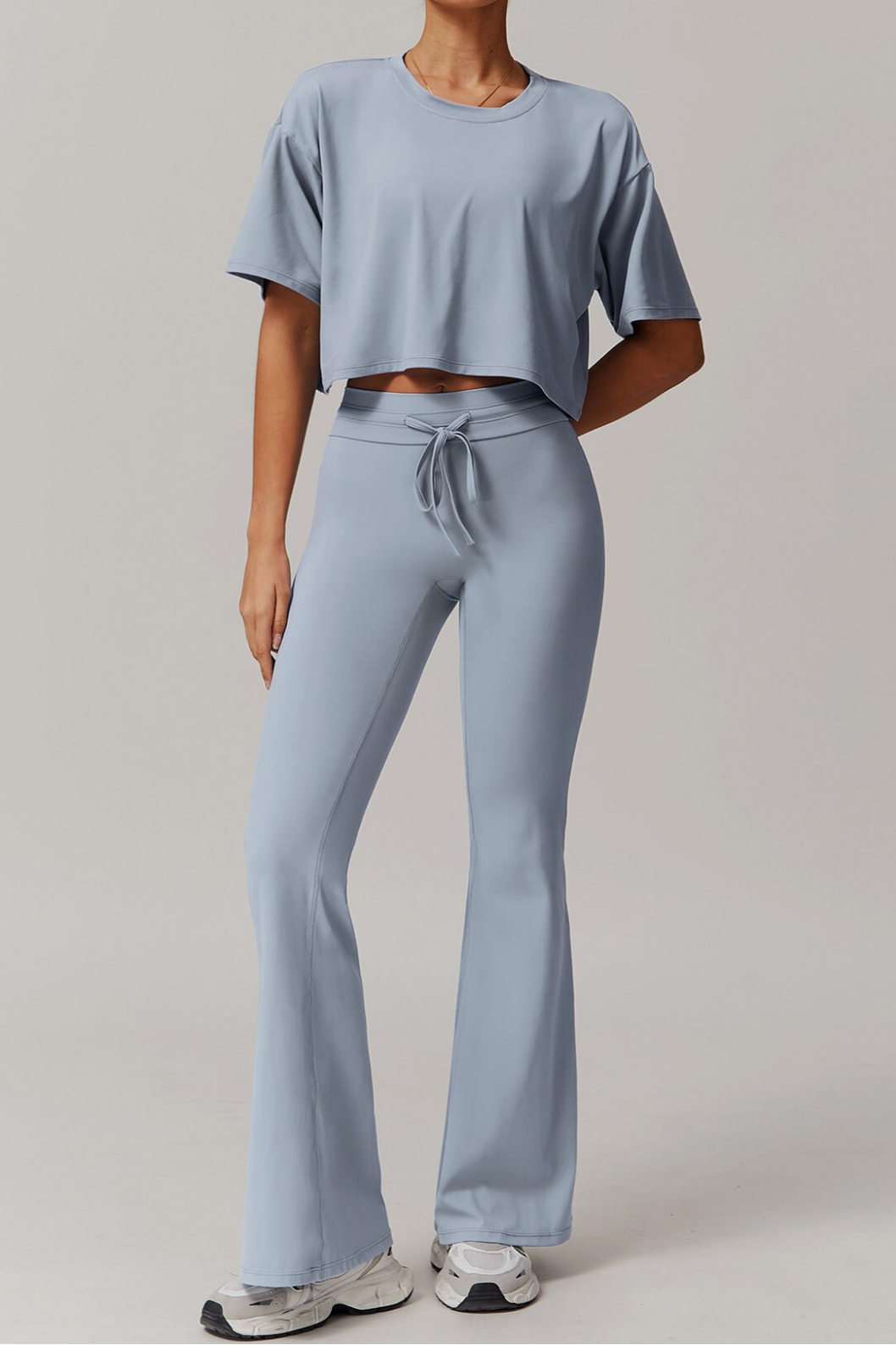 Person wearing a light blue grey outfit with a crop top and flared pants on a plain background