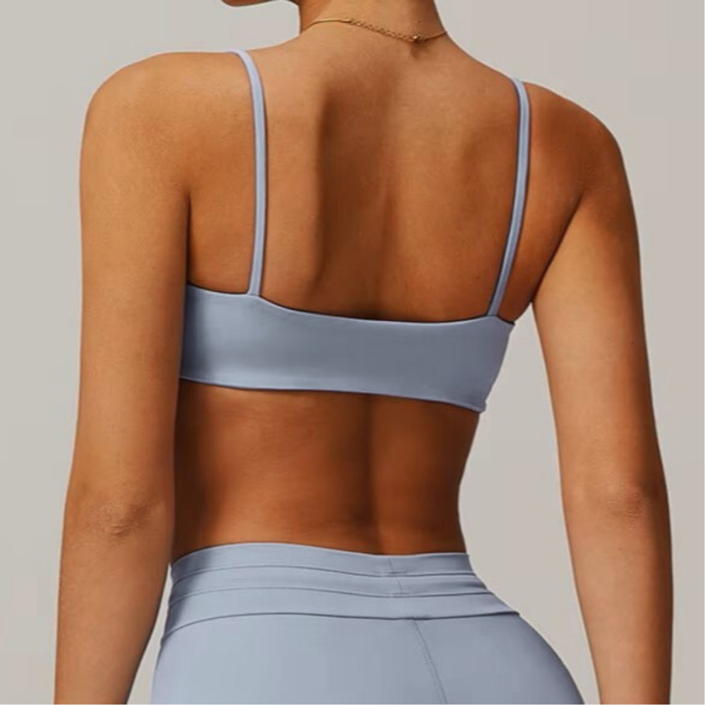 Person wearing a light blue grey sports bra and leggings on a neutral background