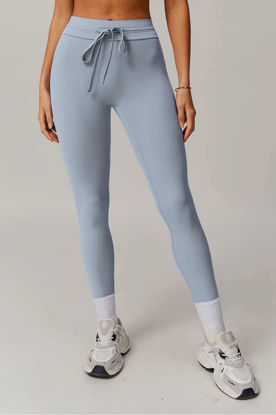 Person wearing light blue grey leggings and white sneakers on a plain background