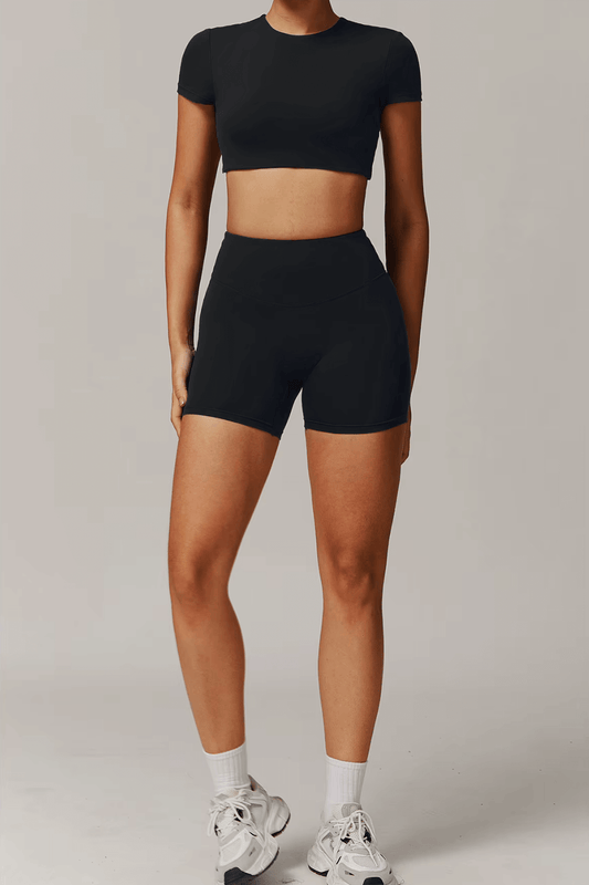 Person wearing a black activewear set  including crop top and shorts with white sneakers on a neutral background
