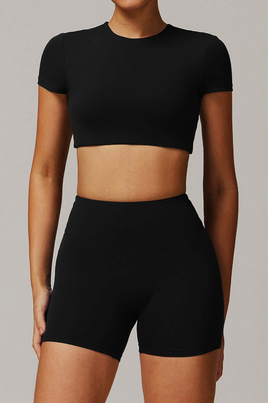 Person wearing a black crop top and black high-waisted shorts on a gray background