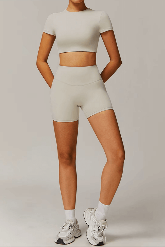 Person wearing a stone activewear outfit with shorts and crop top on a plain background