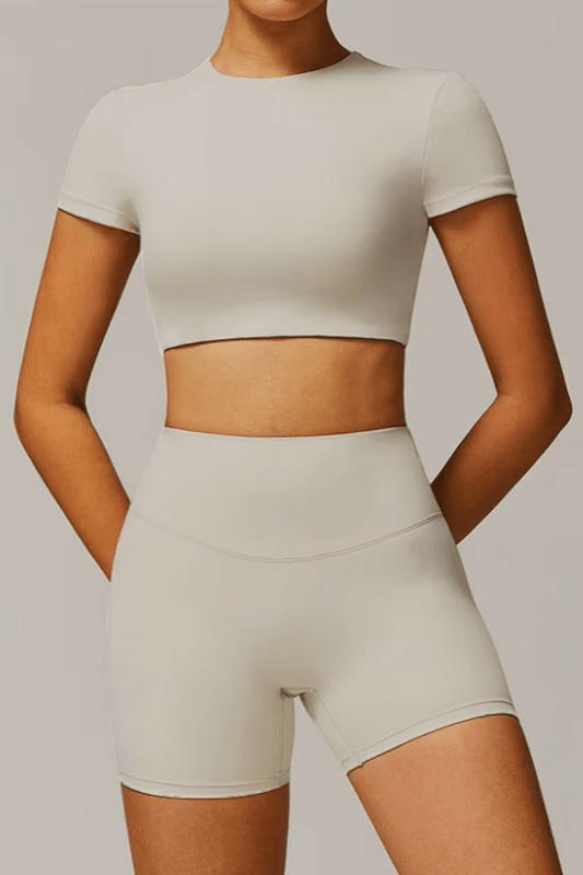 Person wearing a stone color crop top and high-waisted shorts on a plain background