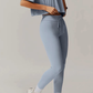 Person wearing a light blue grey athletic outfit with leggings and a crop top on a plain background
