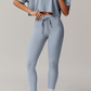 Person wearing a light blue grey athletic outfit with leggings and a crop top on a plain background