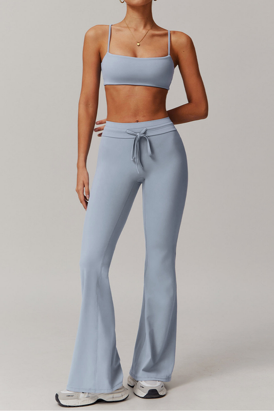 Person wearing a light blue grey athletic outfit with a top and flared pants on a plain background