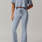 Person wearing a light blue grey outfit with a crop top and flared pants on a plain background