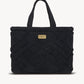 A black cotton tote bag with a unique pom pom design, thick handles, and a canvas-lined interior with a zipper pocket.